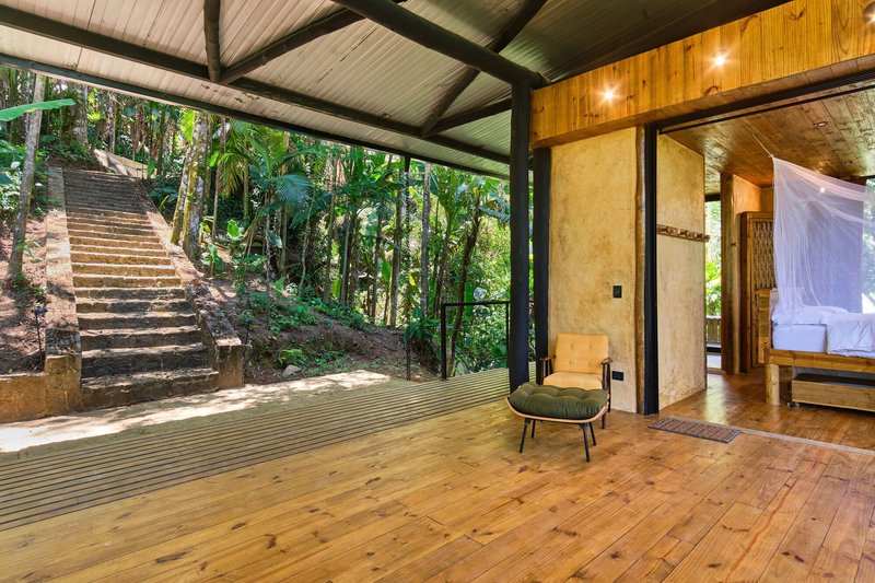 Open-air terrace with timber flooring and exposed steel beams looking toward exterior stairs cutting through the hillside