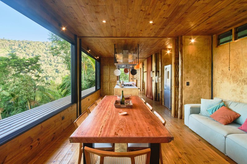 Dining area with timber ceiling and long table overlooking forested hillside through full-height glazing