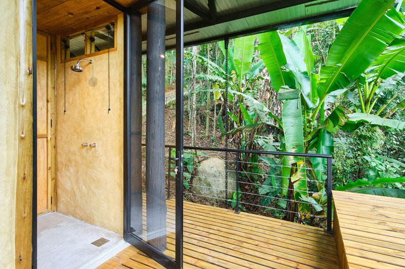 Outdoor shower with plywood wall and steel railing overlooking banana plants