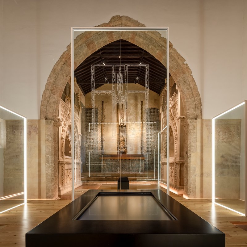 Stone archway framing nave with glass vitrines and timber ceiling at night