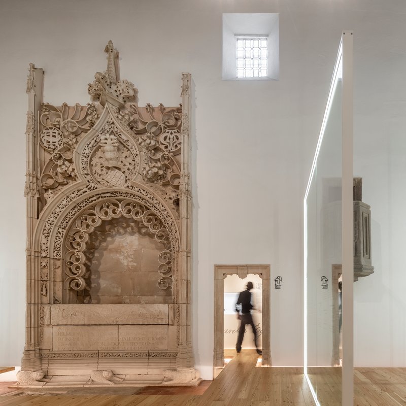 Carved stone portal beside doorway with person walking through backlit opening