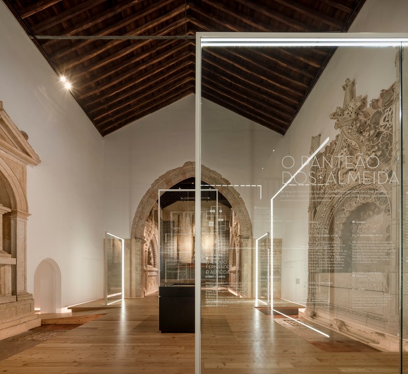 View through glass panels with etched text toward stone arches and dark timber ceiling beams
