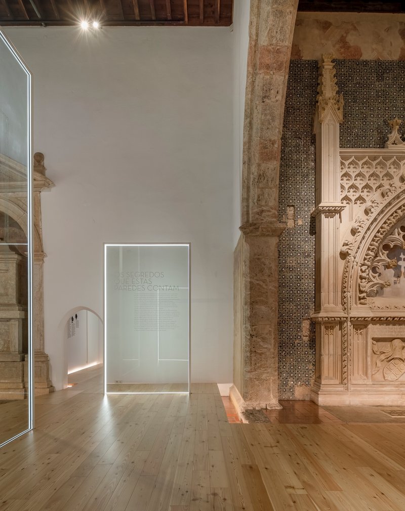 Backlit glass partition with etched inscription standing beside a weathered stone column and tiled wall