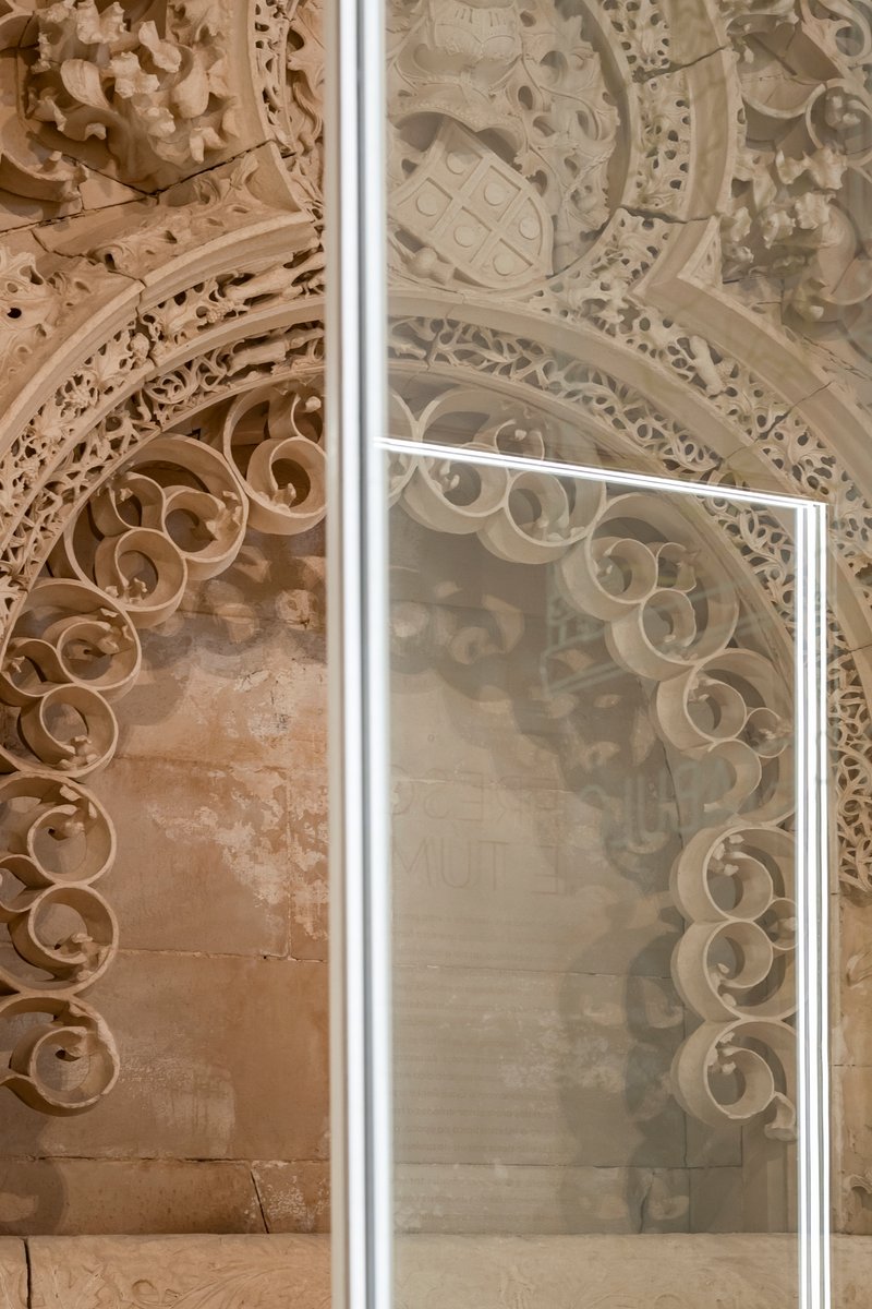 Detail of glass panel edge bisecting ornate carved stonework with decorative scrolls and heraldic symbols