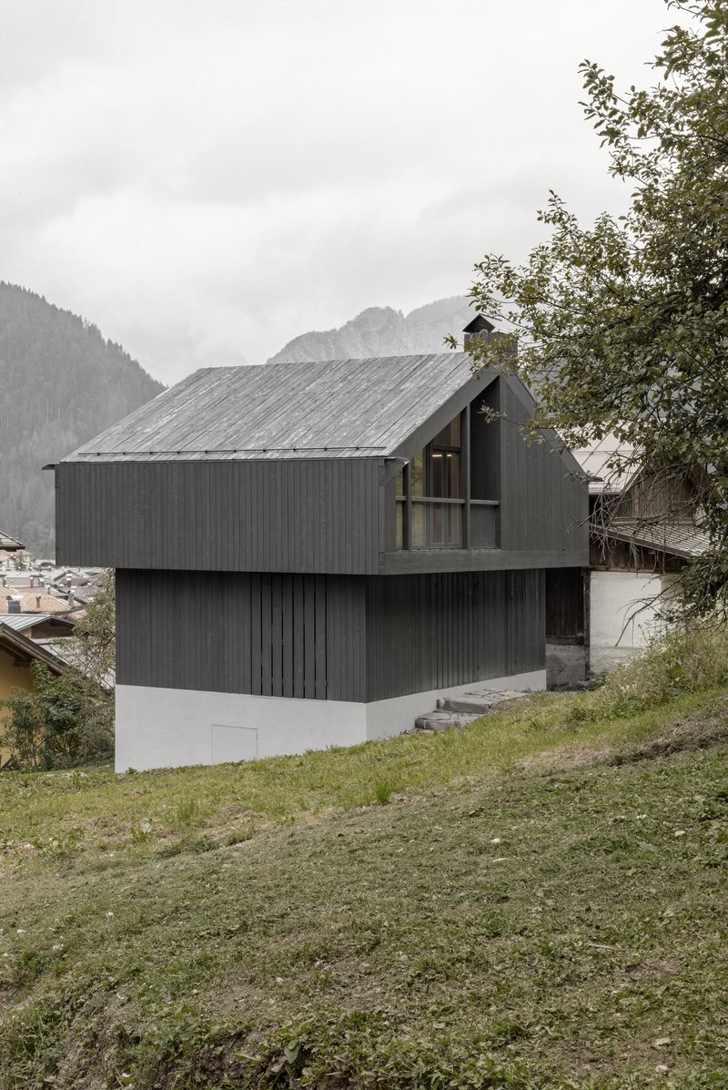 Corner view of dark timber facade with recessed upper balcony framed by deciduous trees