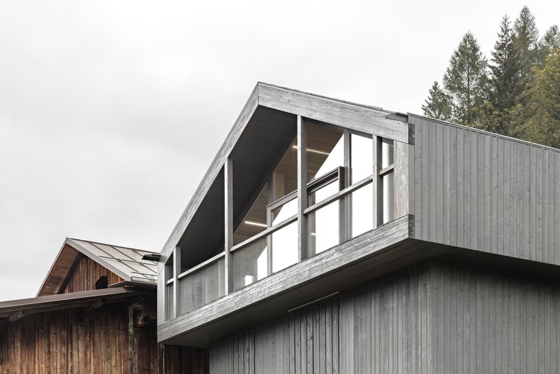 Vertical timber cladding and angled glazed section with exposed beams under an overcast sky