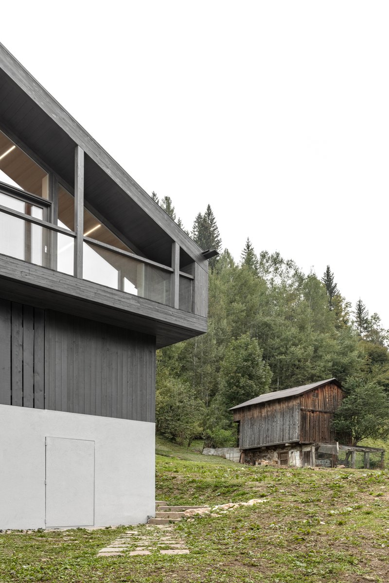 Cantilevered upper volume with full-height windows overlooking a hillside meadow and distant timber barn