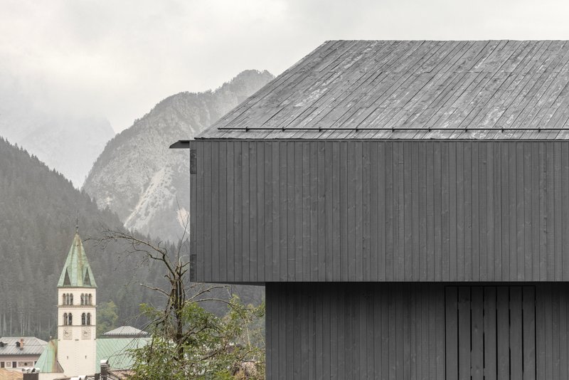 Weathered timber roof and dark wood facade with distant church tower visible through morning mist