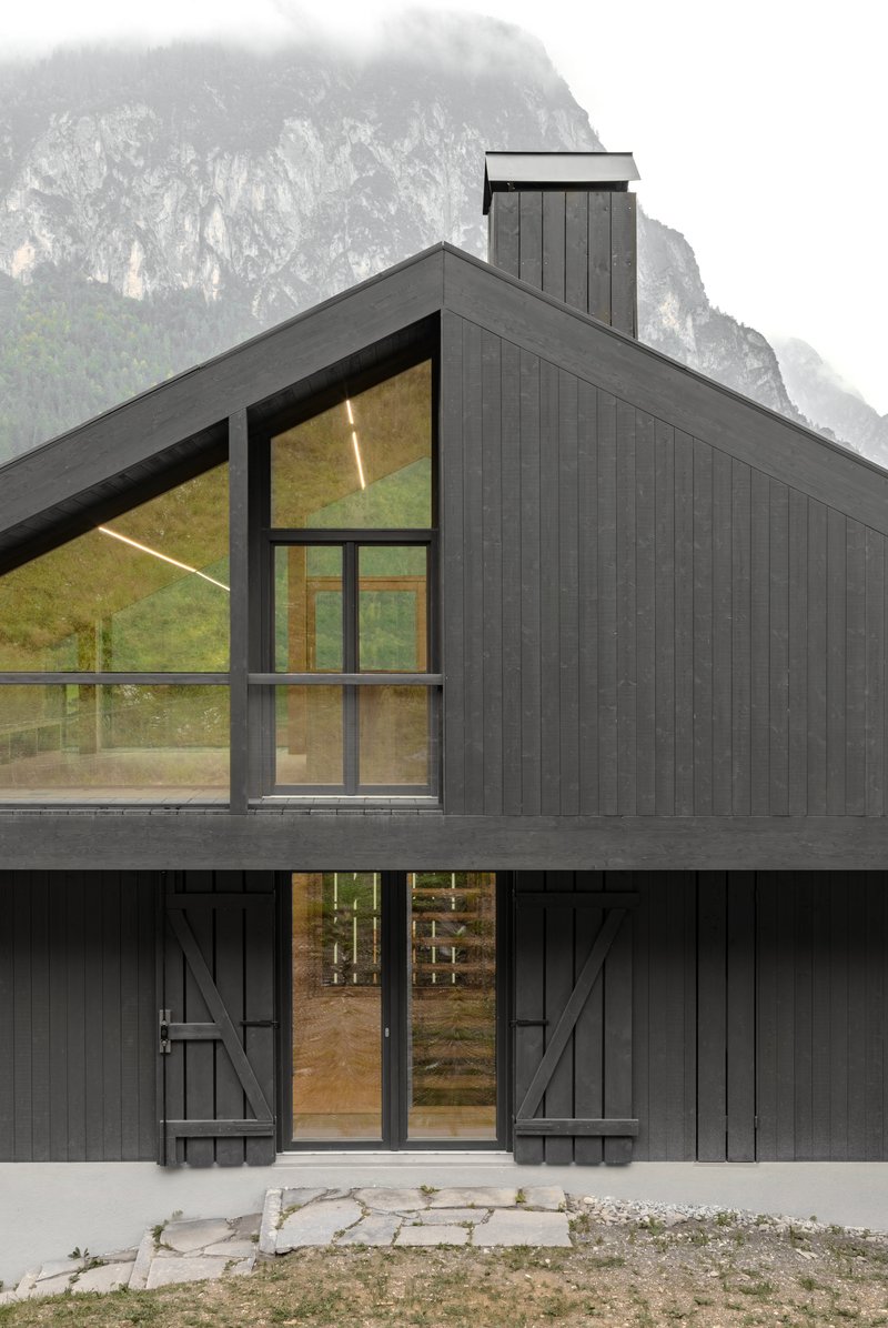 Gabled facade with triangular glazing and diagonal barn doors on the lower level facing the valley