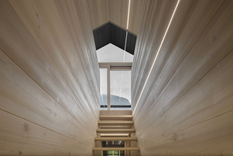 Timber staircase rising toward a pentagonal skylight framed by horizontal plank walls