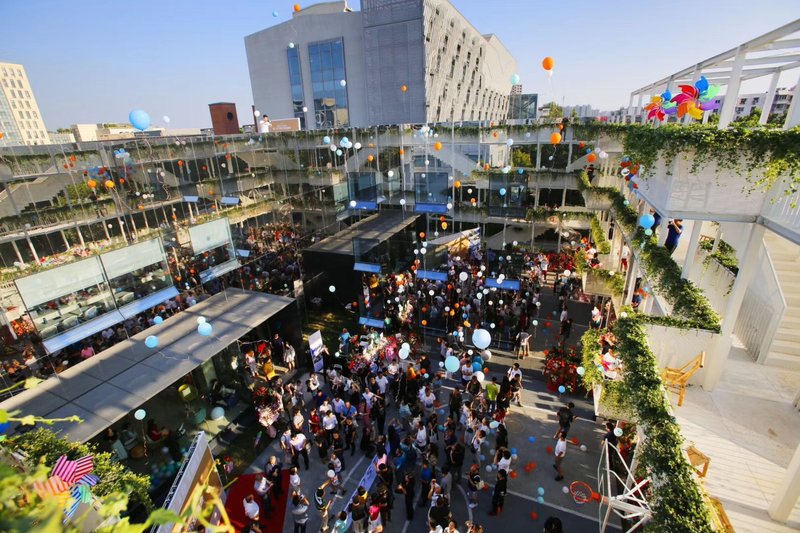 Aerial view of courtyard celebration with balloons rising past terraced units and planted green edges