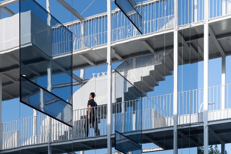 Close-up of external staircases with white railings and a figure walking across a bridge