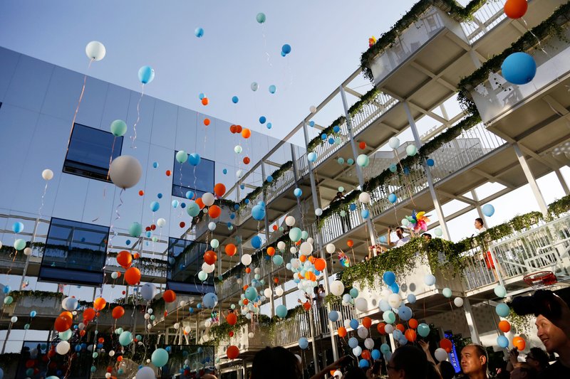 Rising balloons in courtyard framed by planted concrete terraces and white structural columns overhead