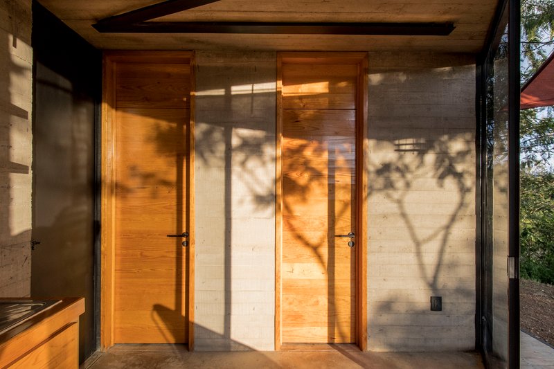 Timber doors in concrete corridor with tree shadows cast across the floor and walls
