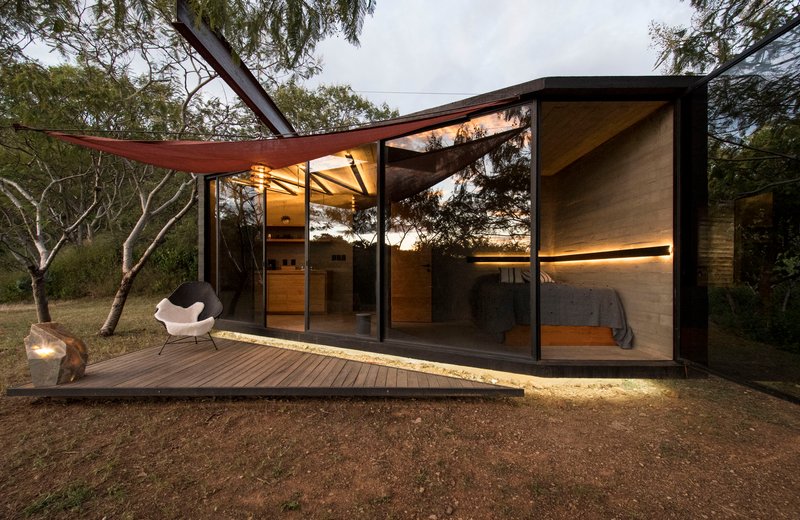 Glass-walled pavilion with cantilevered roof and timber deck illuminated at dusk among scattered trees