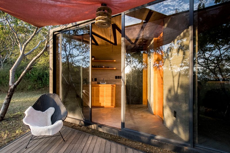 Open glass doors revealing the board-formed concrete interior and spiral stair under dappled afternoon light