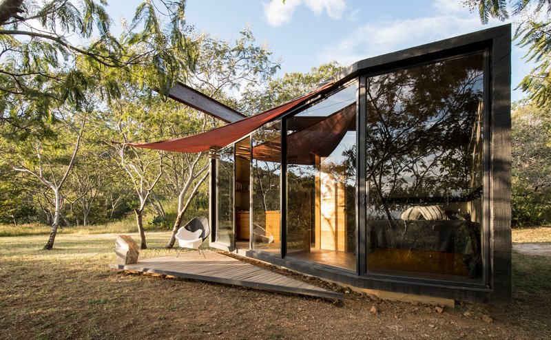 Corner view of the glazed volume with fabric shade canopy suspended above the timber terrace