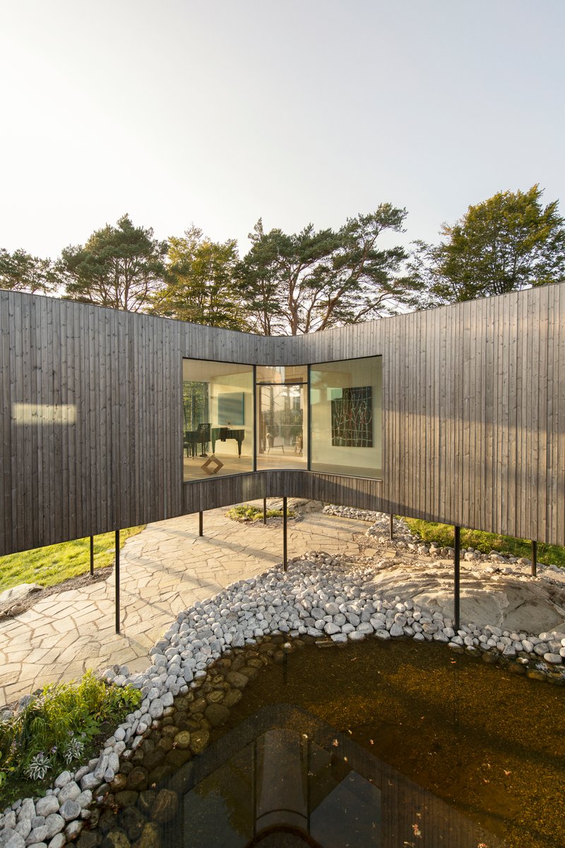 Curved timber facade embracing a courtyard with stone paving and a reflecting pool at dusk