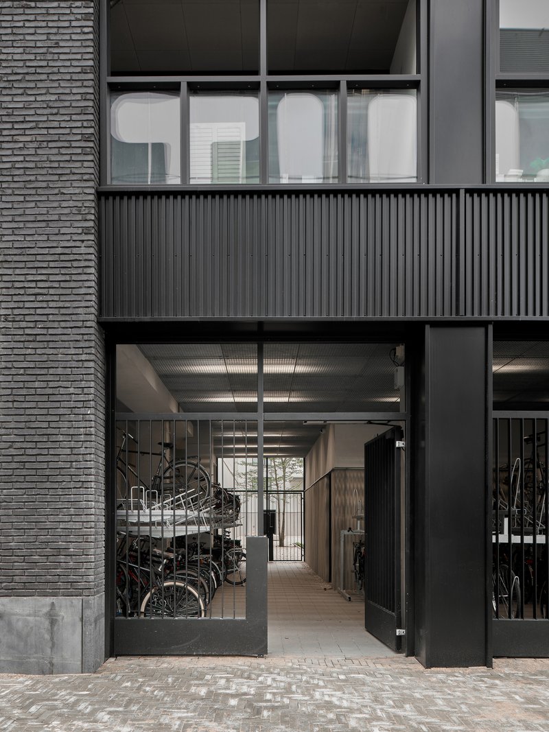 Ground-floor entrance with glazed doors opening to bicycle storage beneath corrugated metal ceiling