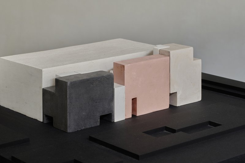 Physical massing model with white, pink, and grey volumes arranged on a black base