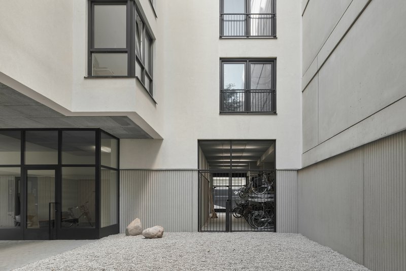 Courtyard with gravel surface, bicycle storage gate, and white rendered walls rising to the sky