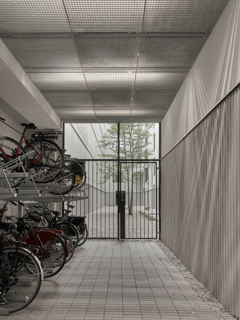 Covered bicycle storage with metal mesh ceiling and glazed gate opening to trees beyond