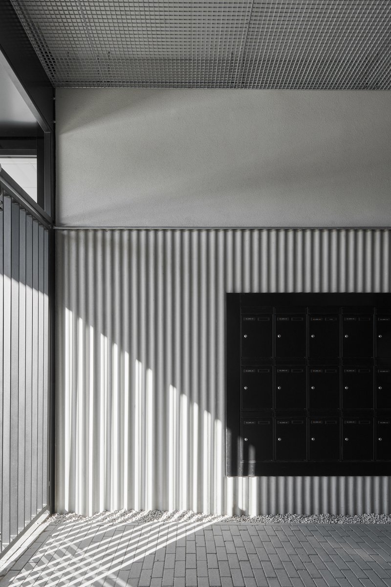 Entry alcove with corrugated metal wall casting striped shadows beside a black mailbox bank
