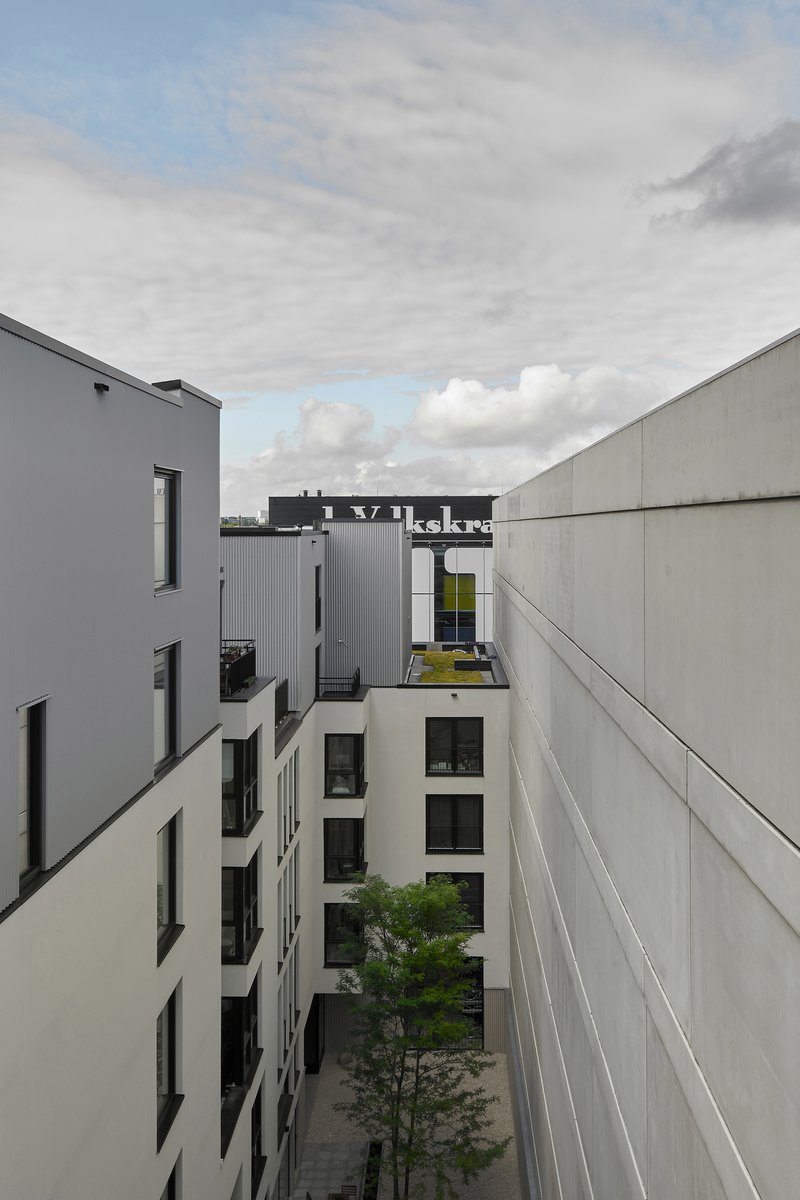 Courtyard view between white and grey facades with a young tree under cloudy skies