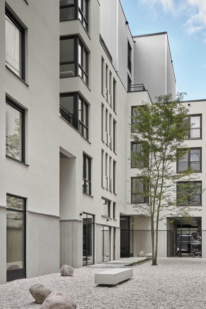 Interior courtyard with white facades, a single tree, concrete bench, and gravel ground