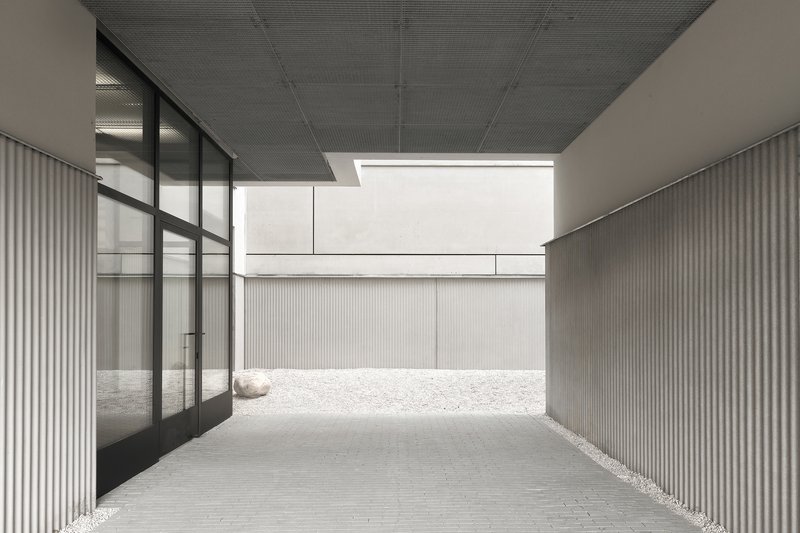 Covered passage with ribbed ceiling and glass wall opening to a gravel courtyard beyond