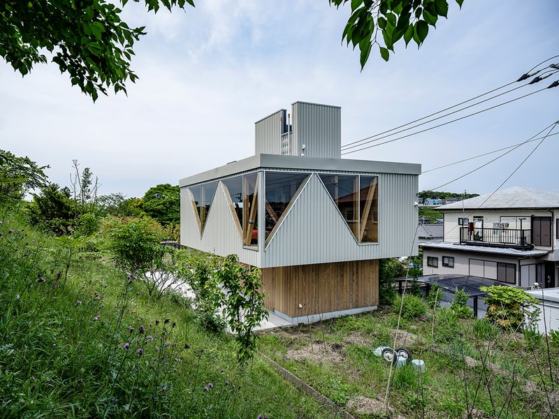 Corrugated metal facade with triangular windows set above a timber base surrounded by green vegetation