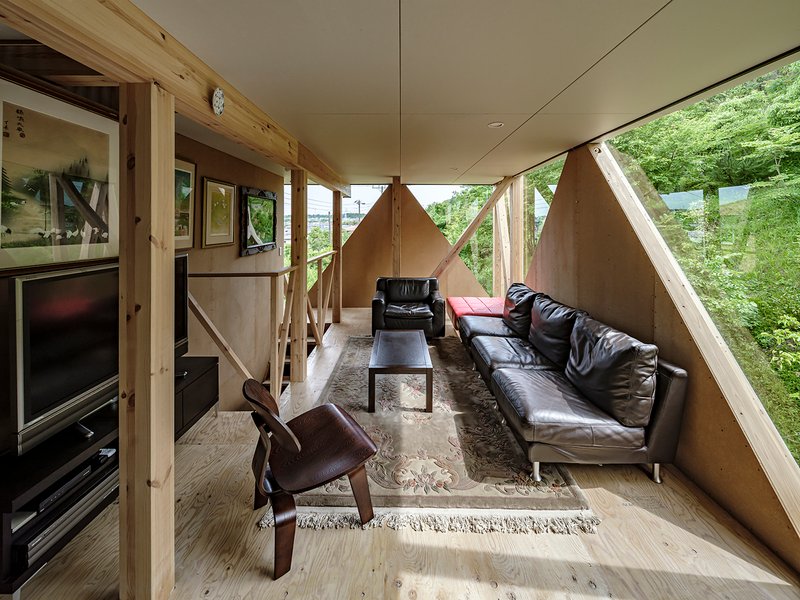Interior living space with exposed timber columns and plywood walls framing views to surrounding greenery