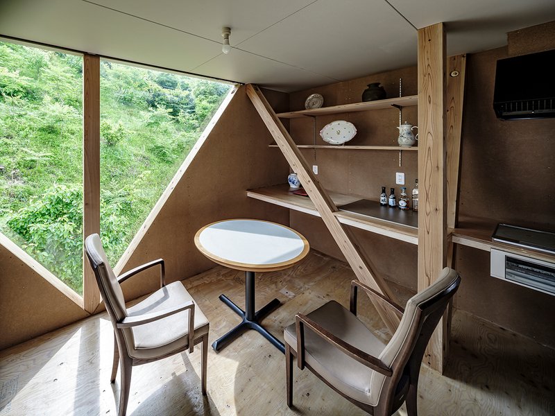 Dining nook with built-in plywood shelving beneath an angled structural timber brace and triangular window