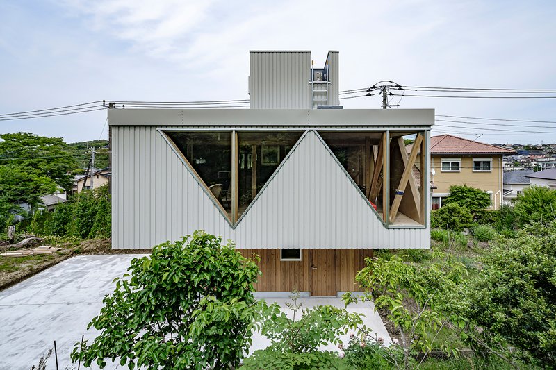 Triangular cutout windows in the corrugated metal facade framing exposed timber diagonal bracing