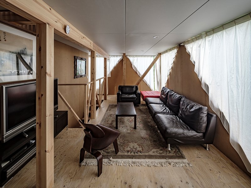 Living room with exposed timber framing, diagonal braces, white curtains and polished concrete floor