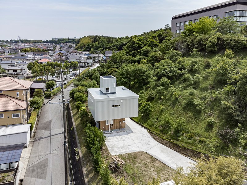 Aerial view of a white metal-clad house with a rooftop tower set on a sloping site above a residential neighborhood