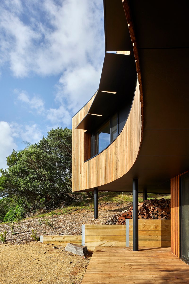 Underside of the curved cantilever showing slot windows and the timber deck below with stacked firewood