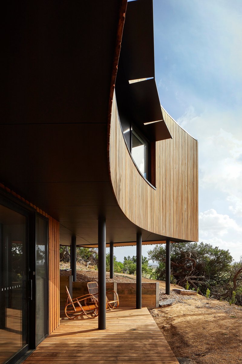 Covered timber deck beneath the cantilevered upper floor with rocking chairs looking toward the hills