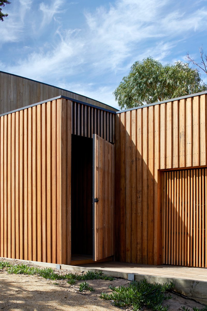 Vertical timber screen facade with recessed entry portal beneath a willow tree