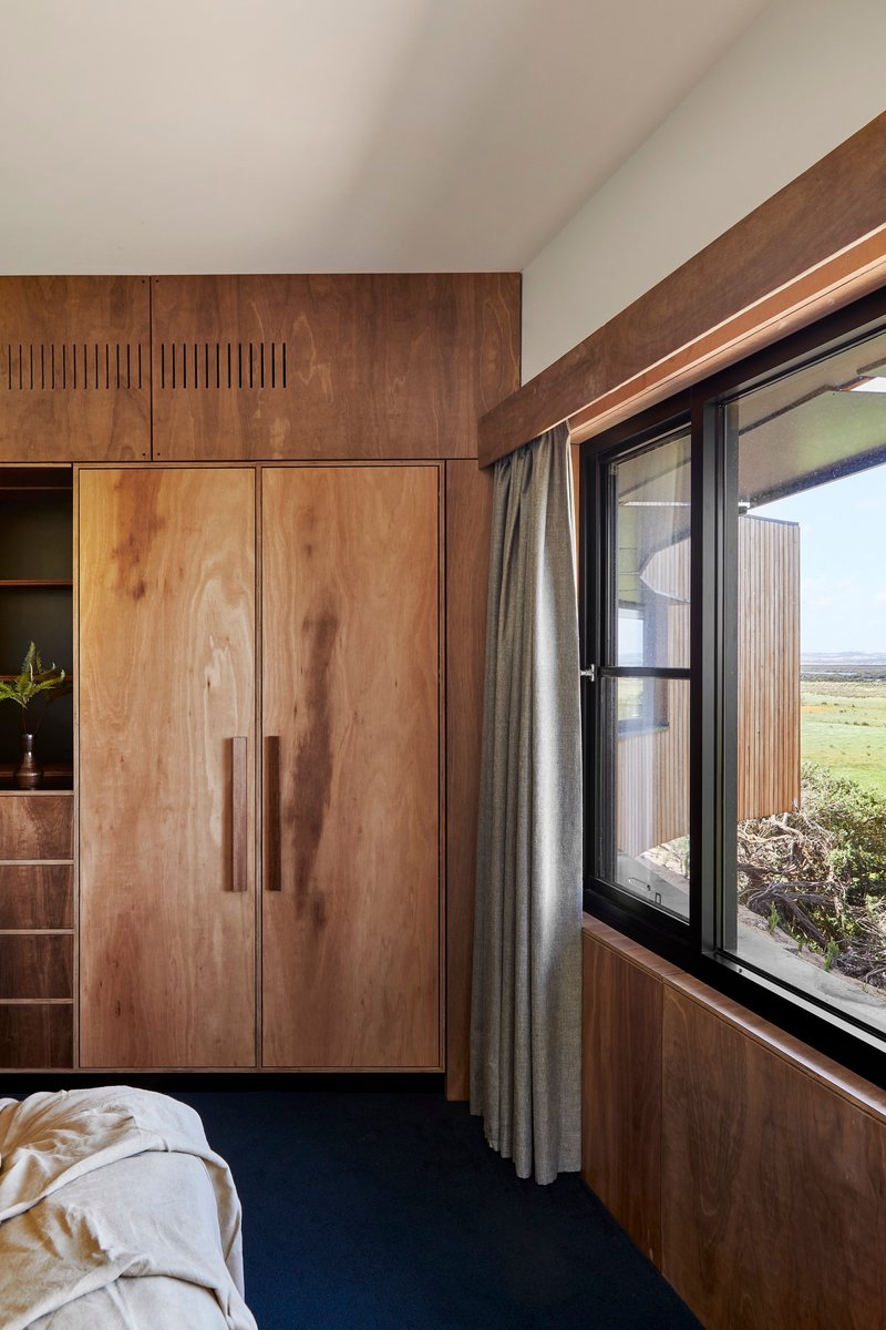 Bedroom with built-in timber cabinetry and corner window overlooking open grassland