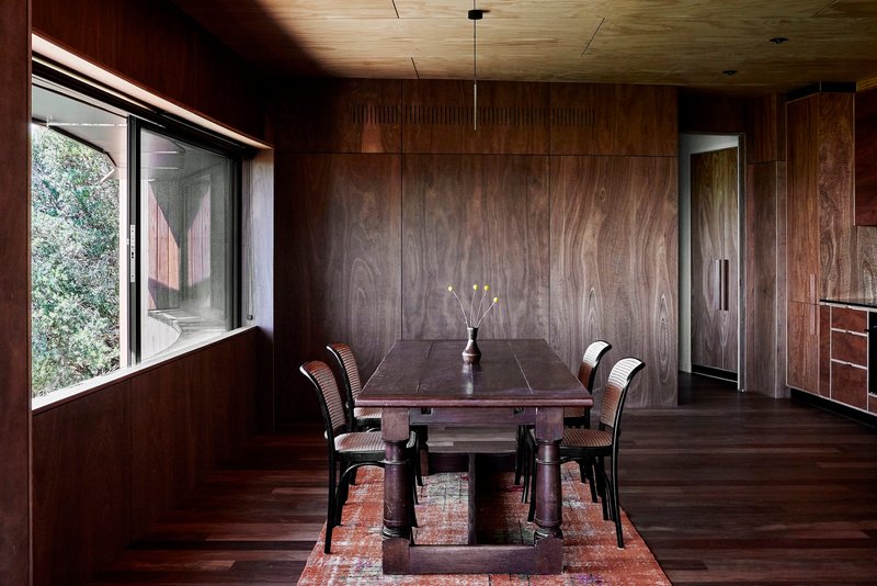 Dining room with dark wood-paneled walls and ceiling lit by a linear fixture