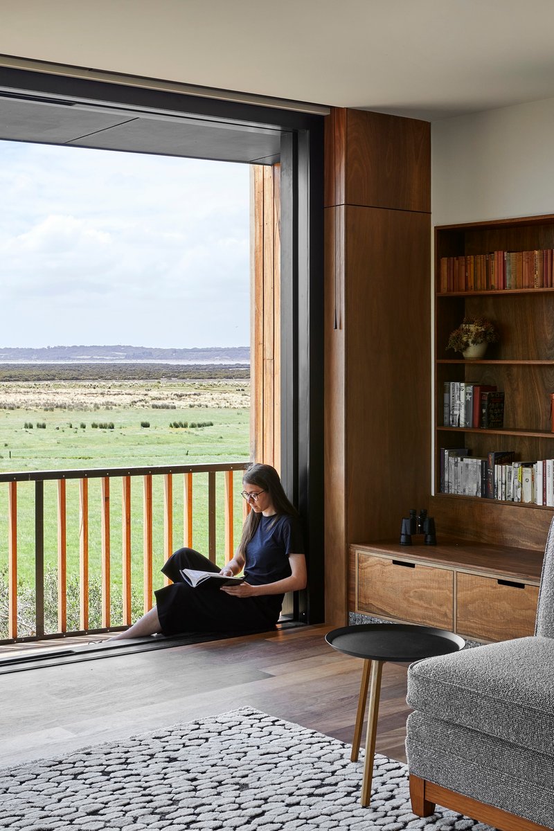 Reading nook beside a sliding door with person seated overlooking expansive green landscape
