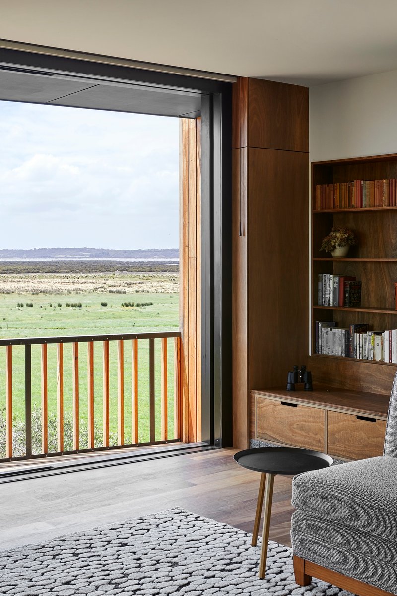 Living room with timber bookshelf beside sliding door opening to a timber-railed balcony