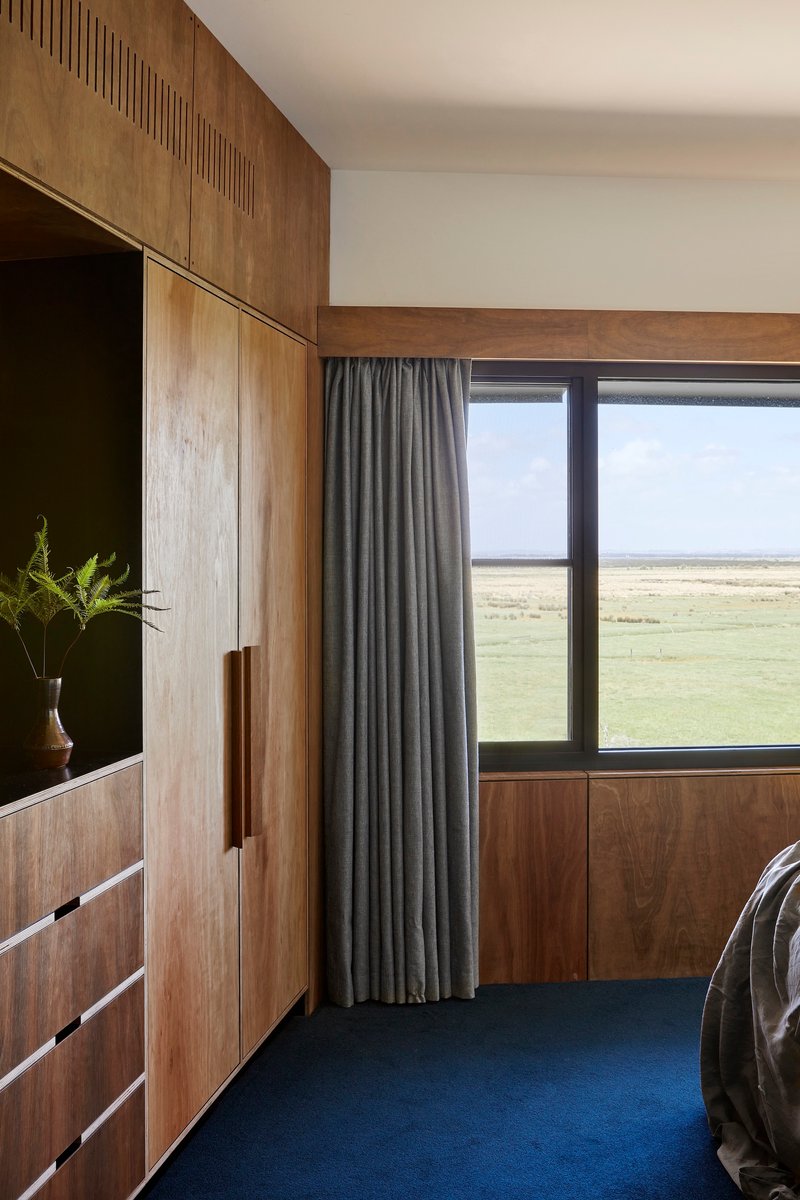 Bedroom with timber built-in cabinetry and grey curtain framing a window overlooking open grassland