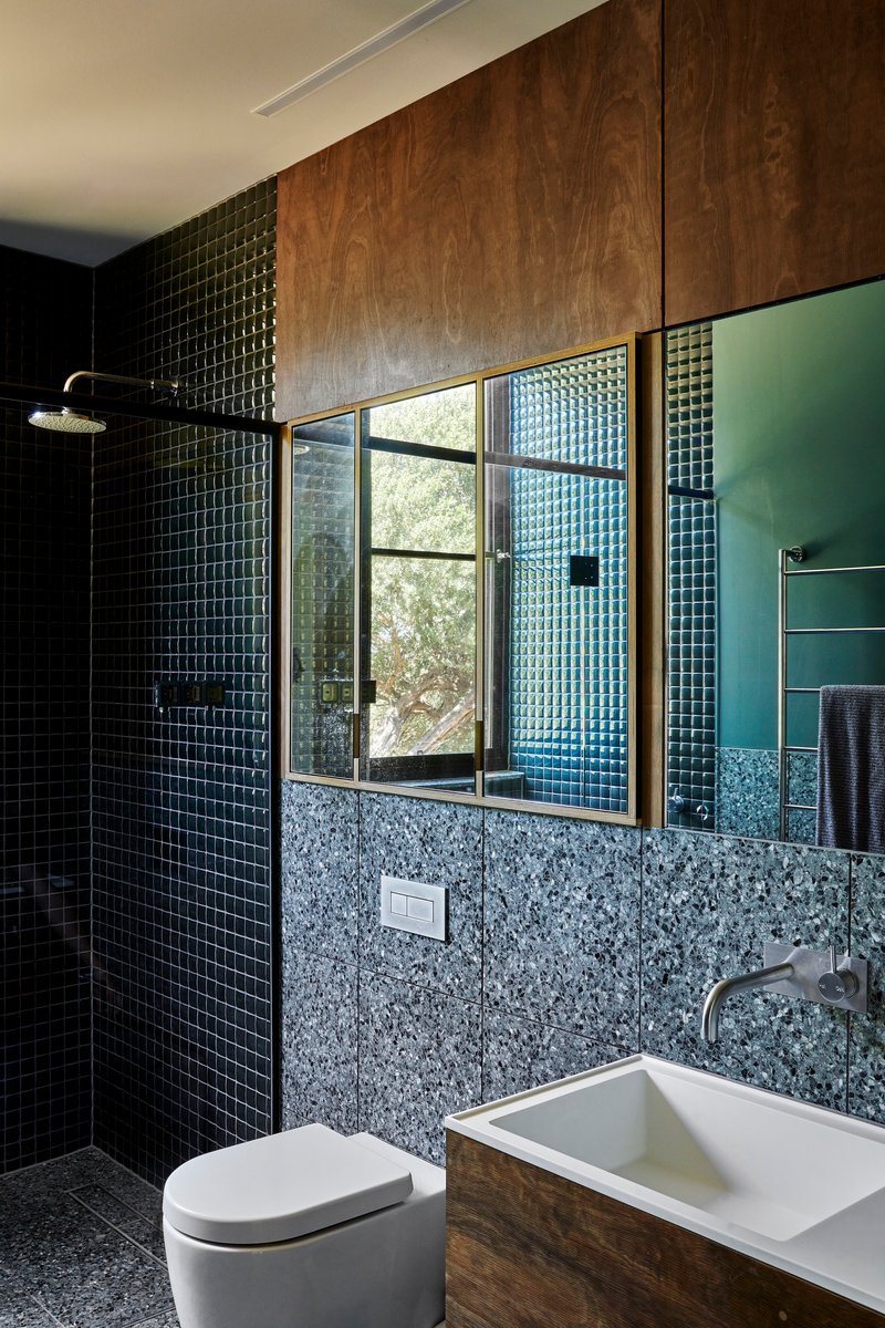 Bathroom with dark mosaic tile walls, terrazzo base, and timber-framed window to greenery outside