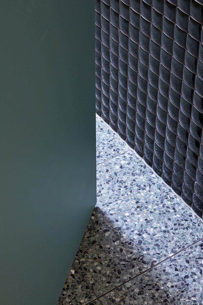 Floor detail where terrazzo meets dark mosaic tile wall with green painted surface adjacent