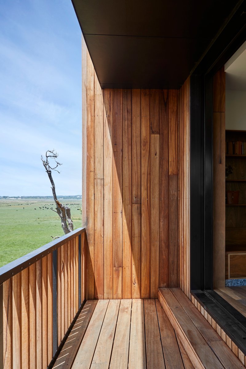 Timber-clad balcony with vertical boarding and decking overlooking a flat green landscape under blue sky