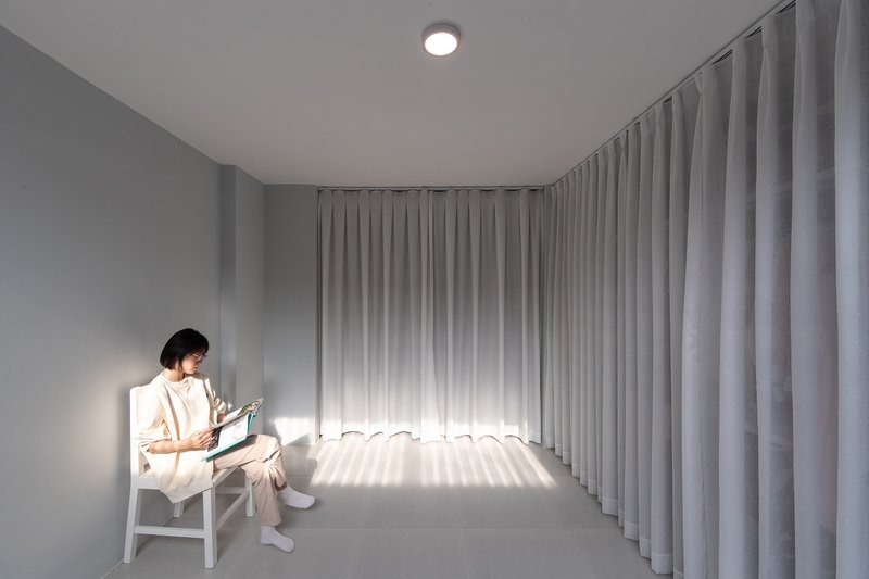 Minimal room with full-height fabric curtains and a person reading in evening light