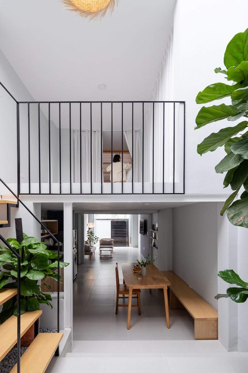 Double-height living space with vertical steel bar mezzanine railing and large potted plants