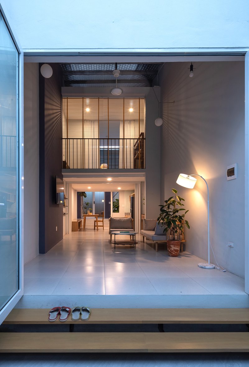 View through open threshold showing double-height interior with timber-slatted upper screen at twilight